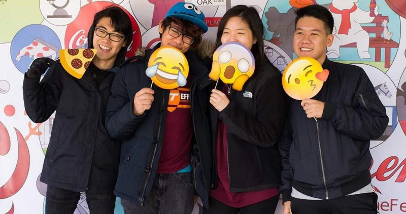 Students holding paper emojiis pose for photos in the Hokies Taste the Feeling booth